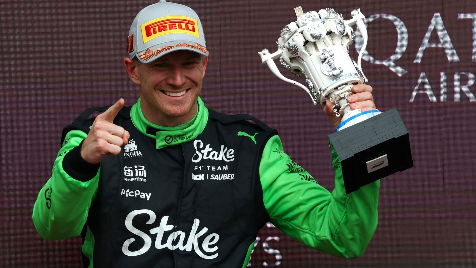Nico Hulkenberg holding a trophy, pointing forward with his right hand while smiling